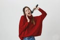 Gorgeous woman with long brown hair enjoying singing, holding a microphone over white background. Girl definitely knows