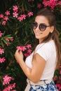 Gorgeous woman in sunglasses stand in beautiful flowers. Portrait of happy smiled young woman