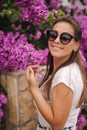 Gorgeous woman in sunglasses stand in beautiful flowers. Portrait of happy smiled young woman