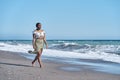 gorgeous young African American woman strolling along the beach in a summery skirt