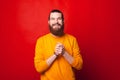 A gorgeous young bearded man is looking cheerful at the camera near a red wall Royalty Free Stock Photo