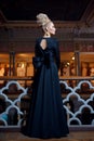 Gorgeous young blonde model, dressed in a long black dress with bow at the back, elegant hairstyle, crown and earrings. Royalty Free Stock Photo