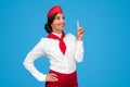 Gorgeous young flight attendant in red and white uniform pointing up and smiling Royalty Free Stock Photo
