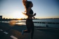 Gorgeous young girl with long brown hair dressed in sports clothes runs on the road along the reservoir on the sunset