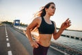 Gorgeous young girl with long brown hair in a sports top and tights runs on the road along the reservoir on the sunset