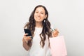 Gorgeous young lady smiling at the camera is holding a light pink shopping bag and her phone. Royalty Free Stock Photo