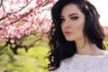 gorgeous young woman in elegant dress posing in garden with blossom peach trees
