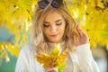 Gorgeous young woman looks down at yellow autumn leaves in her hands standing under the mapel tree