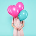 Gorgeous young woman in party outfit holding bunch of colourful balloons, isolated over pastel blue colored background. Birthday.