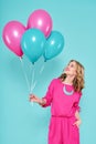 Gorgeous young woman in party summer dress holding bunch of colourful balloons, isolated over pastel blue colored background.