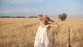 Gorgeous young woman in white dress runnung in the wheat field. Smiling, happy female running and holds her straw hat on