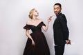 Gorgeous young woman in evening dress with flower looking impishly at handsome man in tuxedo with present behind his Royalty Free Stock Photo