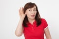 Gossip concept. Portrait of pretty middle aged woman with palm near her ear. Red blank polo shirt. Copy space Royalty Free Stock Photo