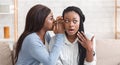 Young black girl whispering secret to her shocked friend`s ear