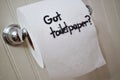 `Got Toilet Paper`, written in sharpie on cardboard toilet paper roll that is left hanging on the spool, on the wall