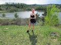 Goth informal girl in a black dress with pink hair on a background of a lake and nature from the mountain