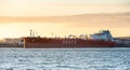 Red oil tanker ship unloading at an oil refinery at sunset..