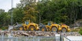 Three yellow Volvo wheel loaders parked by a forest..