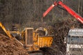 Crane loading bushes and trees into an industrial wood chipper..