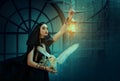 Gothic fantasy woman witch in black dress cape, hood. Girl princess dark magician holds vintage lamp lantern in hand