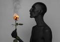 Gothic and Halloween theme: a man with black skin holding a red rose, black death isolated on a gray background in studio