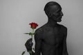 Gothic and Halloween theme: a man with black skin holding a red rose, black death isolated on a gray background in studio Royalty Free Stock Photo