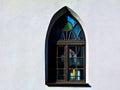 Gothic shape church window with pointy arch and colorful glass in white stucco wall Royalty Free Stock Photo