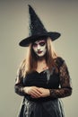 Gothic young woman in witch halloween costume with hat standing over gray background, woman in carnival costume of witch or dead Royalty Free Stock Photo