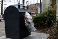 Gouda, South Holland/The Netherlands - February 15 2020: Plastic waste bag hanging on a container for collecting trash being left