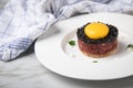 Gourmet beefsteak Tatar with lean raw beef filet, capers, egg yolk, onions, toast bread, black caviar on porcelain plate on light