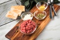 Gourmet beefsteak Tatar with lean raw beef filet, capers, egg yolk, onions, toast bread on wooden board and light marble