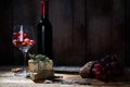 Gourmet composition of wineglass with grapes and walnuts on wood table with cheese and bottle of red wine. Copy space