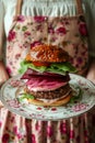 Gourmet Homemade Beef Burger with Lettuce and Onion on Vintage Floral Plate Held by Person in Apron