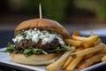 Gourmet lamb burger with arugula, feta cheese, and tzatziki sauce on a freshly baked ciabatta bun, served with garlic fries