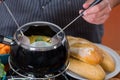 Gourmet Swiss fondue dinner with assorted cheeses and a heated pot of cheese fondue, man holding with a fork dipping a Royalty Free Stock Photo