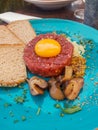 Gourmet tartar raw beef tenderloin with egg yolk and pickled boletus as a close-up on a modern design plate.