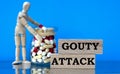 GOUTY ATTACK words on a wooden block on a blue background with pills and a wooden man