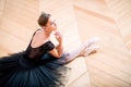 Graceful ballerina in black tutu rests sitting on floor with her back to the camera