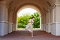 A graceful ballerina girl poses in an ancient street architectural arch. The beauty of an artistic dancer in a light lace dress