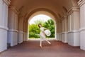 A graceful ballerina girl poses in an ancient street architectural arch. The beauty of an artistic dancer in a light lace dress