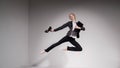 Graceful barefoot ballerina in a business suit jumping with shoes in her hands on a white background.