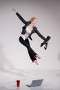Graceful barefoot ballerina in a business suit jumping with shoes in her hands on a white background.
