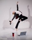 Graceful barefoot ballerina in a business suit jumping with shoes in her hands on a white background.