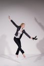 Graceful barefoot ballerina in a business suit jumping with shoes in her hands on a white background.