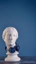 Graceful beautiful plaster Aphrodite in huge round blue headphones, on a vintage wooden table.