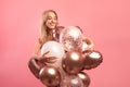 Graceful blonde birthday lady posing with colorful balloons over pink studio background