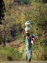 Graceful and strong woman carrying her baby and water containers on her head in Purushwadi.