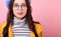 Graceful girl in a stylish beret hat and a yellow cloak in glasses, close-up on a pink background Royalty Free Stock Photo