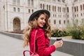 Graceful white woman in gray hat looking over shoulder while exploring old part of city. Photo of playful girl in red