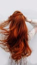 Graceful woman runs fingers through vibrant red hair, white backdrop